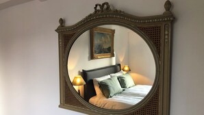 Un dormitorio con un espejo grande y ornamentado, una cama con almohadas y dos lámparas de noche.
