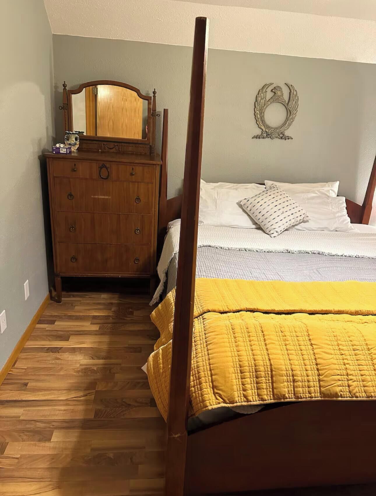 Ein Schlafzimmer mit einem hölzernen Schminktisch, einem Bett mit gelber Steudecke und einem an der Wand befestigten Dekorationselement.