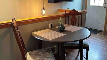 Un comedor con una mesa redonda, dos sillas, un televisor montado en la pared y una puerta con ventana.