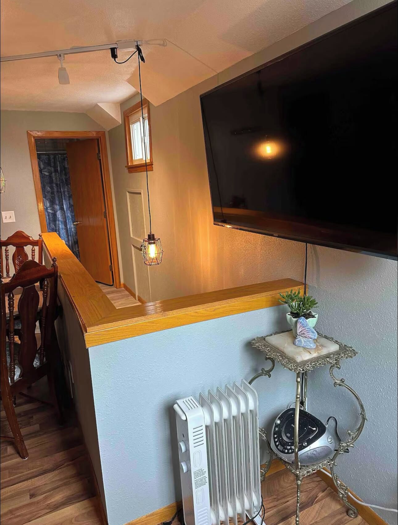 Una sala de estar con una televisión de pantalla plana montada en la pared, una mesa de centro de madera, un radiador y una pequeña planta en maceta.