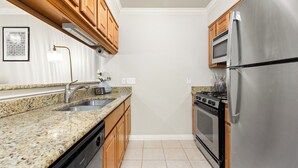 A kitchen with granite countertops, wooden cabinets, stainless steel appliances, and a tiled floor. - 
Travis Heights Modern Getaway - Corporate Housing Rental (Austin)