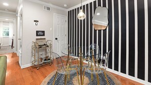 A room with a black and white striped wall, a round glass table with chairs, a gold-framed mirror, and a gold-framed bookcase. - 
Travis Heights Modern Getaway - Corporate Housing Rental (Austin)