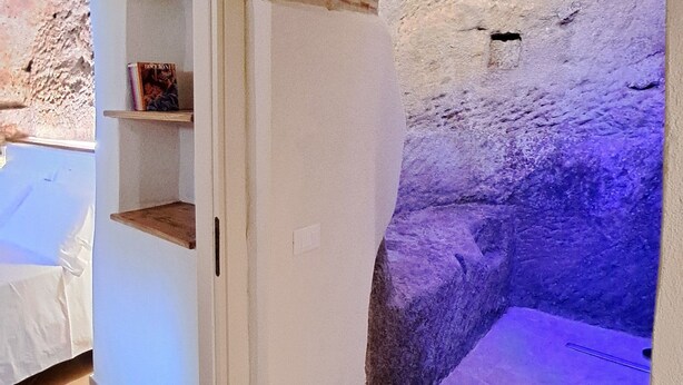 A room with a tiled floor, a white door, a brick wall, and a shelf with books. - Cozy and elegant B&B in the historic center of Belmonte. (Belmonte Calabro)