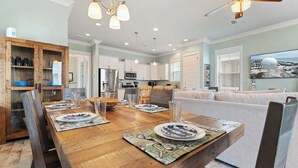 Un coin repas avec une table en bois dressée pour quatre personnes, une cuisine en arrière-plan et un ventilateur de plafond.