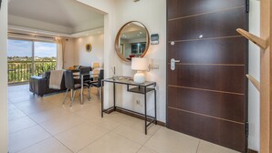 A hotel room with a balcony, a desk with a lamp, a large mirror, and a wooden door.
