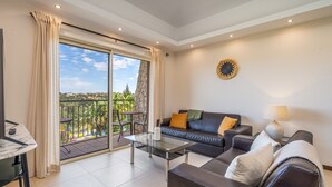 A living room with a glass coffee table, a sofa, a lamp, and a view of a balcony with outdoor furniture.