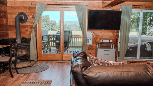A cozy cabin interior with a fireplace, leather sofa, and a dining area with outdoor seating.