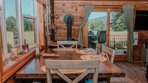 A wooden dining table with woven placemats, wooden chairs, and a view of the outdoors through large windows.