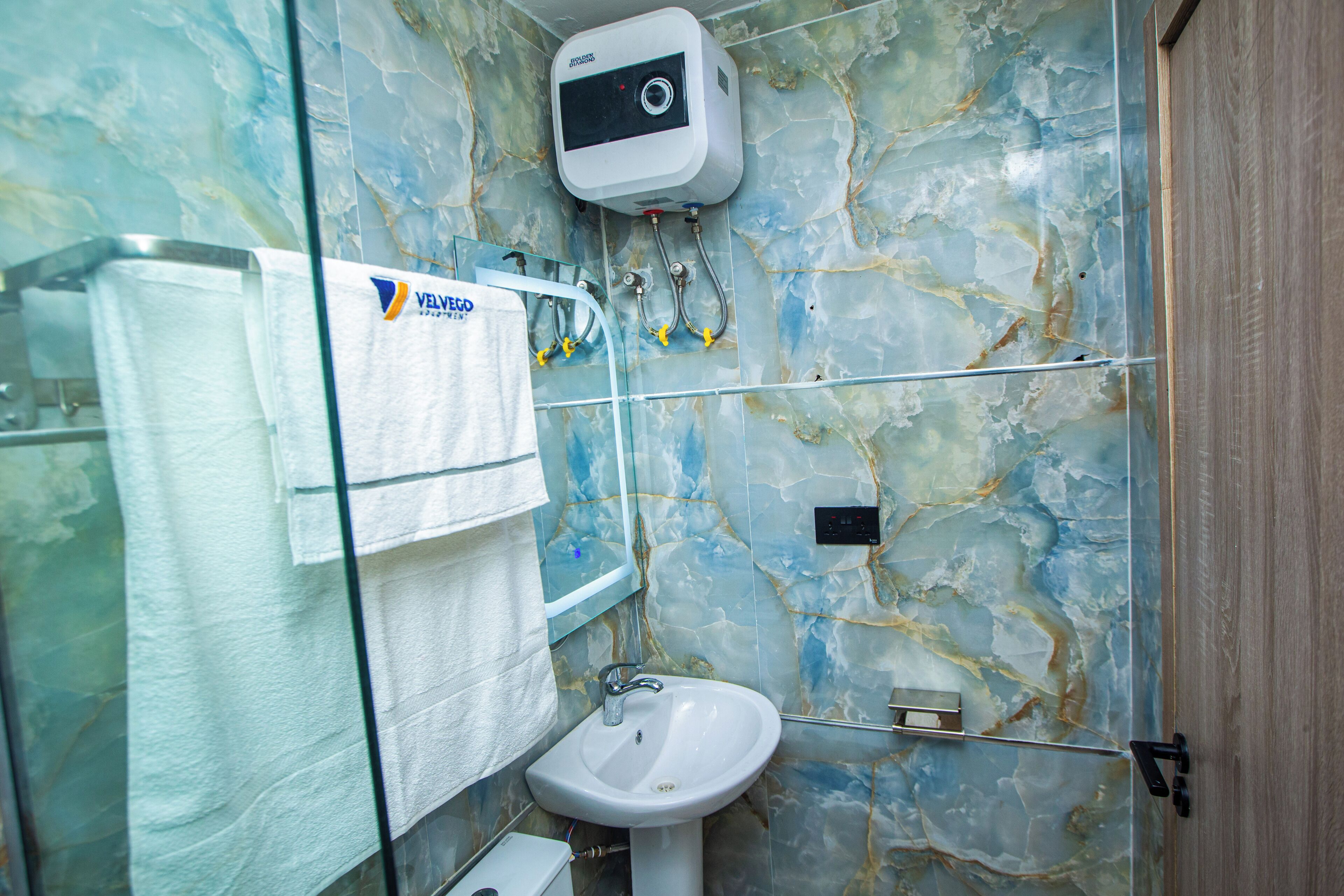 Un baño con pared de mármol, un lavabo blanco y una toalla colgada en un perchero.