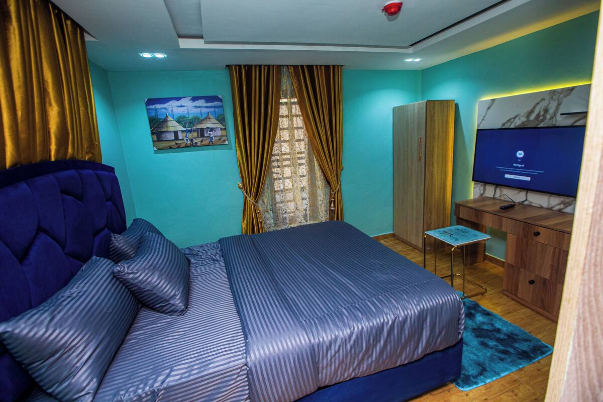 Um quarto com uma cama, uma escrivaninha, um guarda-roupa e uma televisão.