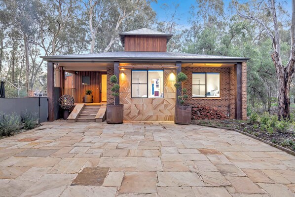A modern house with a stone patio, wooden exterior, and large windows.