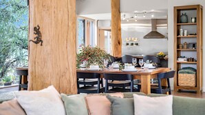 A modern dining area with a wooden table set for four, surrounded by black chairs. A large wooden column with a small animal carving is visible. - The Treehouse (Moama)