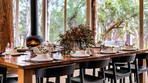 A dining table set for six with white plates, glasses, and a centerpiece of green foliage. - The Treehouse (Moama)