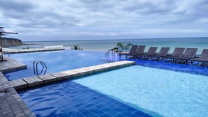 A infinity pool with a view of the ocean, lounge chairs, and a clear sky. - Apartment Ocean Side View Poseidon Building (Manta)