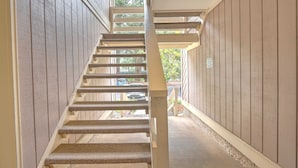 A wooden interior staircase with a handrail, leading to an outdoor area with a car parked outside.