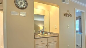 A bathroom with a large mirror, a clock, and a 'BEACH' sign.