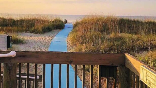 A wooden boardwalk leading to a beach with a blue path.