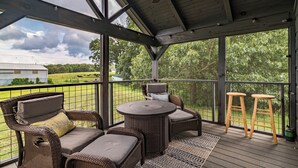 Un espacio de estar techado al aire libre con mobiliario de mimbre y una mesa, con vistas a un paisaje cubierto de césped.