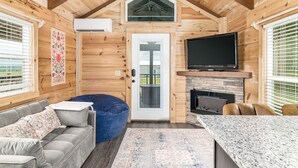 Interior acogedor de una cabaña con detalles de madera, un sofá, un sillón informal, un televisor y una chimenea.