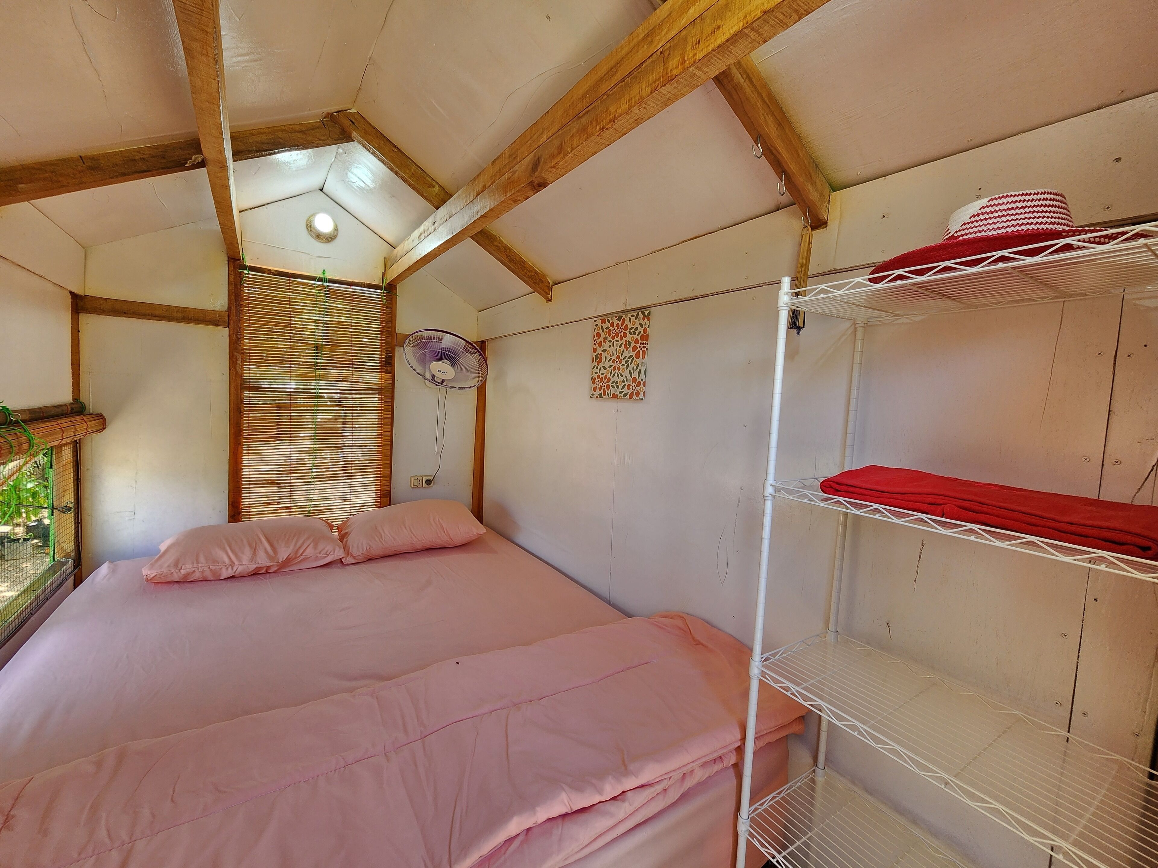 Una habitación con una cama litera, una cama individual, un ventilador, una ventana con persianas y un estante pequeño con un sombrero.