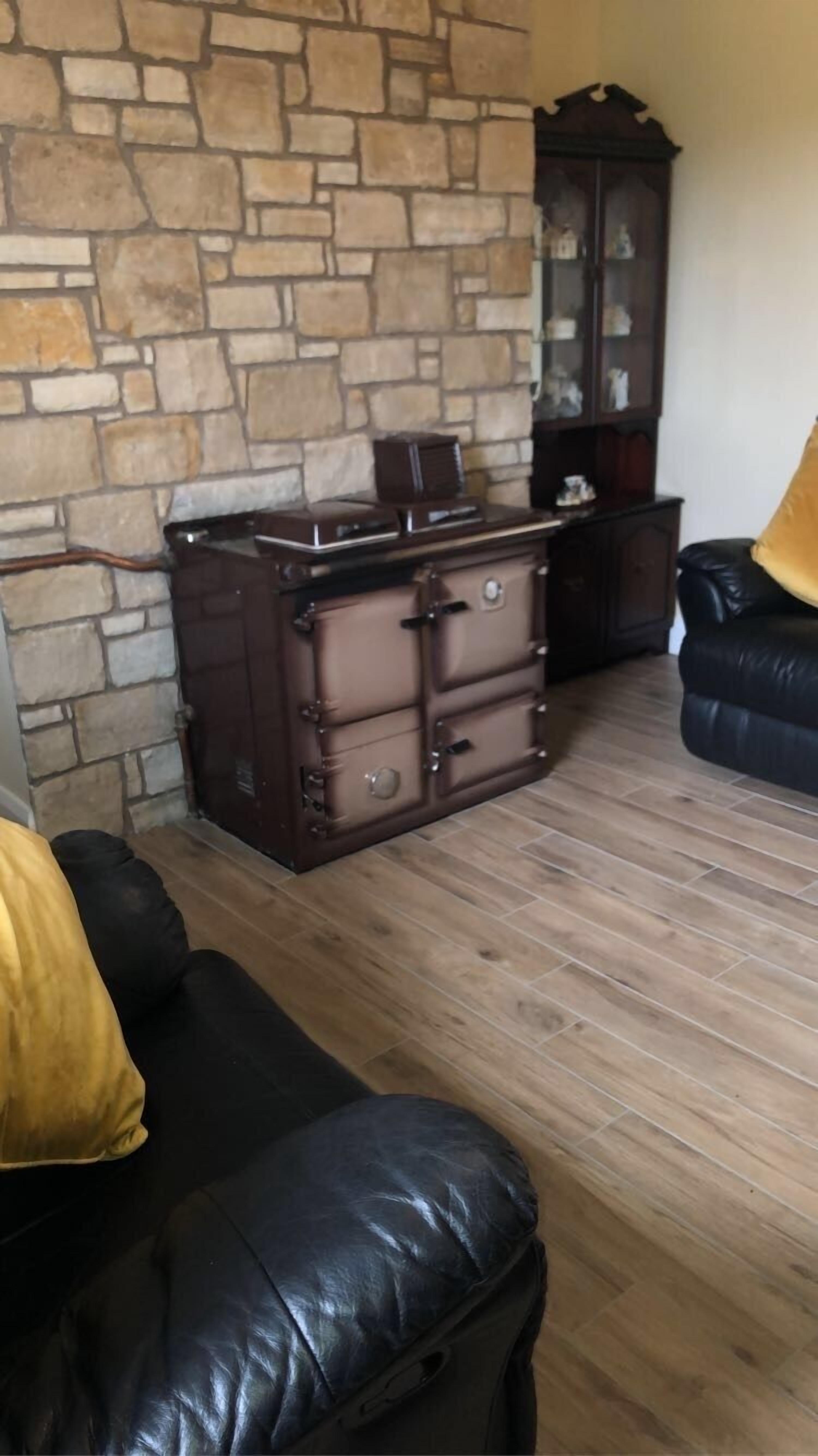 A room with a stone wall, a wooden cabinet, a leather sofa, and a wooden floor.