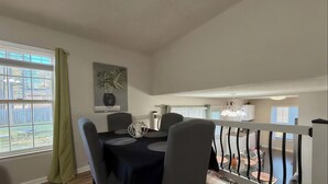 A dining area with a table, chairs, a potted plant, and a view of the backyard.