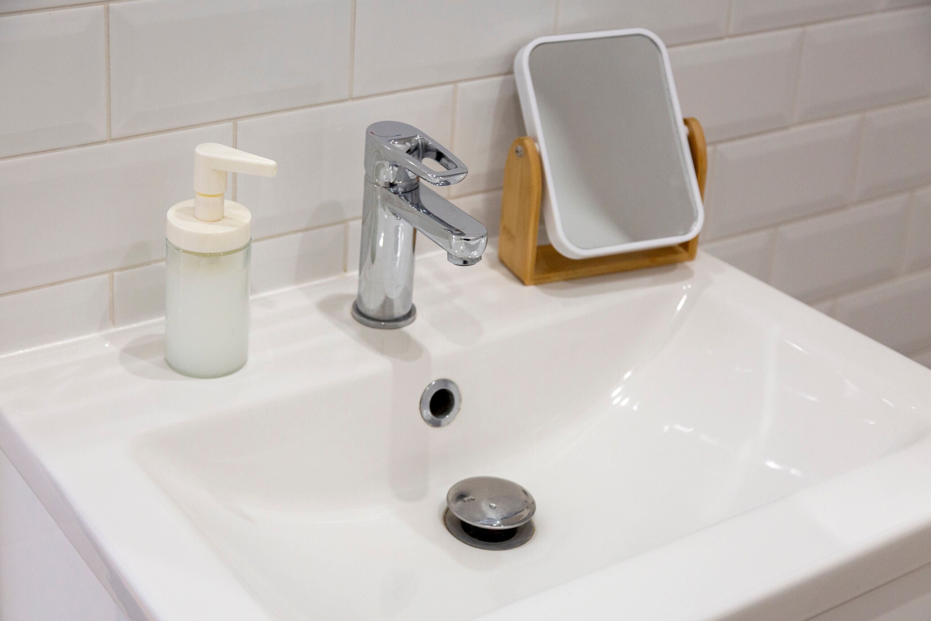 A bathroom sink with a chrome faucet, a soap dispenser, and a mirror on a wooden stand.