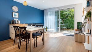 A modern kitchen with a dining area, a clock, and a view of a garden through large windows.