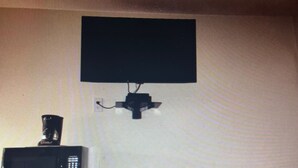 A room with a microwave on a shelf, a small table with a green object on it, and a black object on the wall.