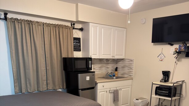 A compact bedroom with a bed, a kitchenette, a desk, and a chair.