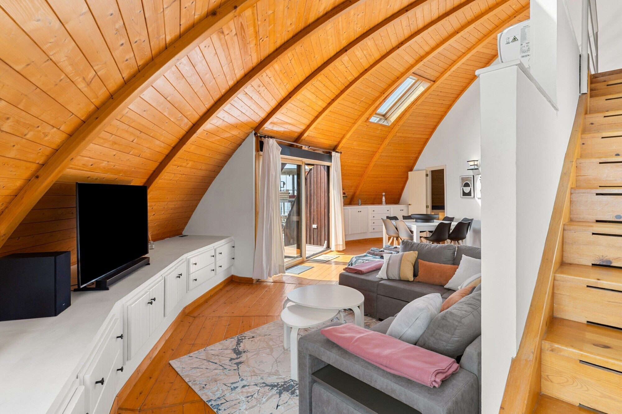 Una camera in stile loft con soffitto spiovente, TV a schermo piatto, divano, tavolo da pranzo e angolo cottura.