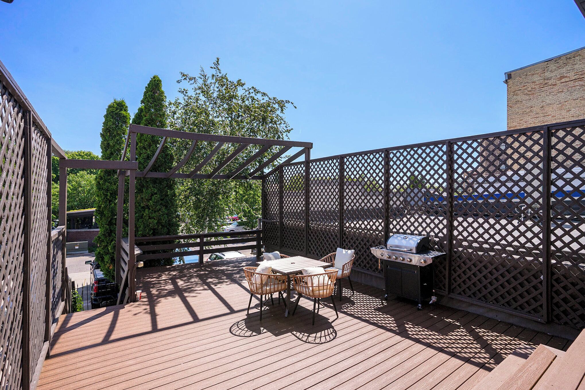 A wooden deck with a table and chairs, a grill, and a lattice fence.