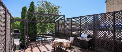 A wooden deck with a table and chairs, a grill, and a lattice fence.