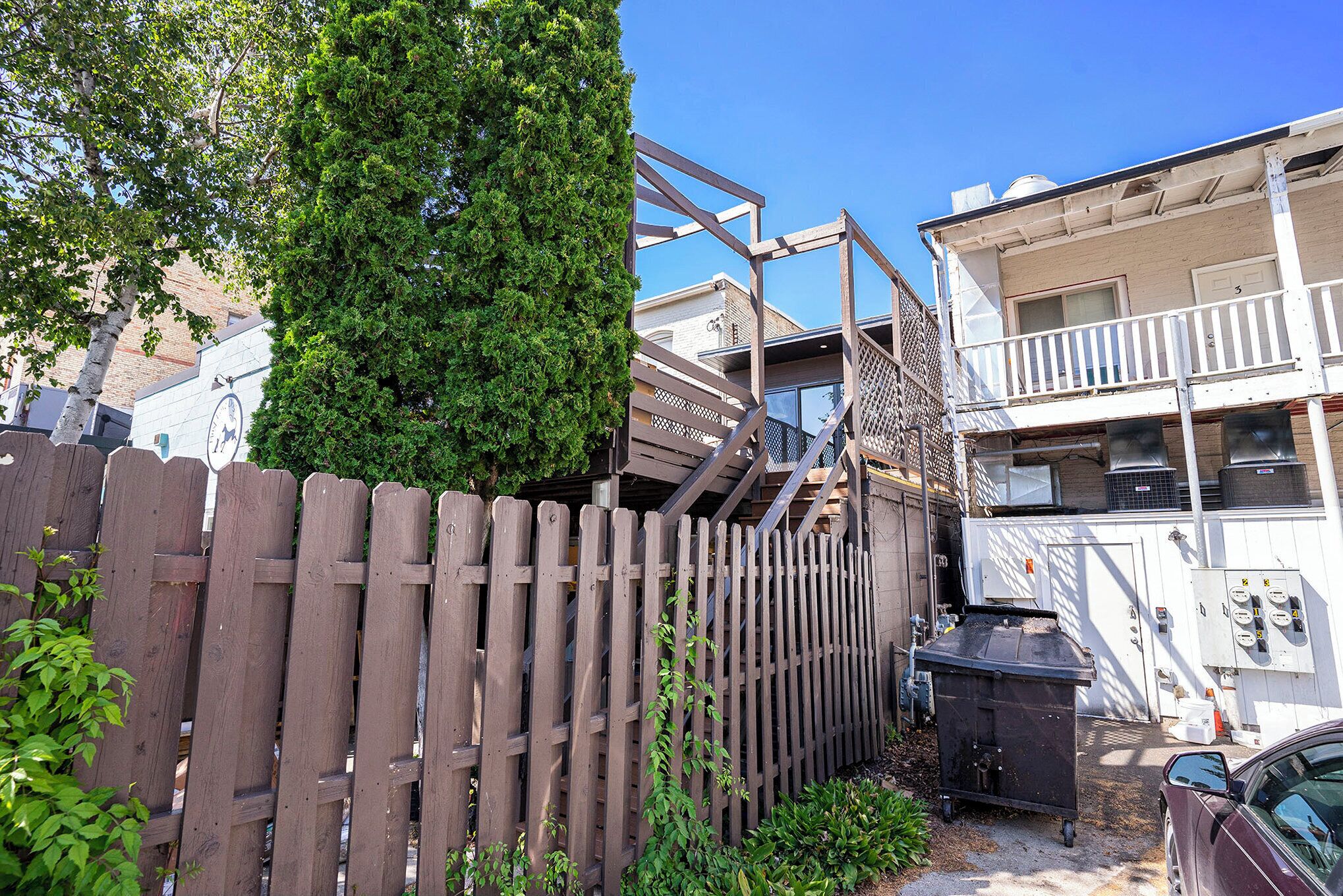 A residential building with a wooden fence, a staircase, and a dumpster.