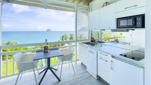 Een moderne keuken met uitzicht op de oceaan, witte kastjes en een kleine eethoek met een tafel en stoelen.