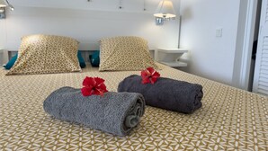Een hotelkamer met een bed met een geborduurd sprei, twee kussens, een nachtkastje en een wandlamp.