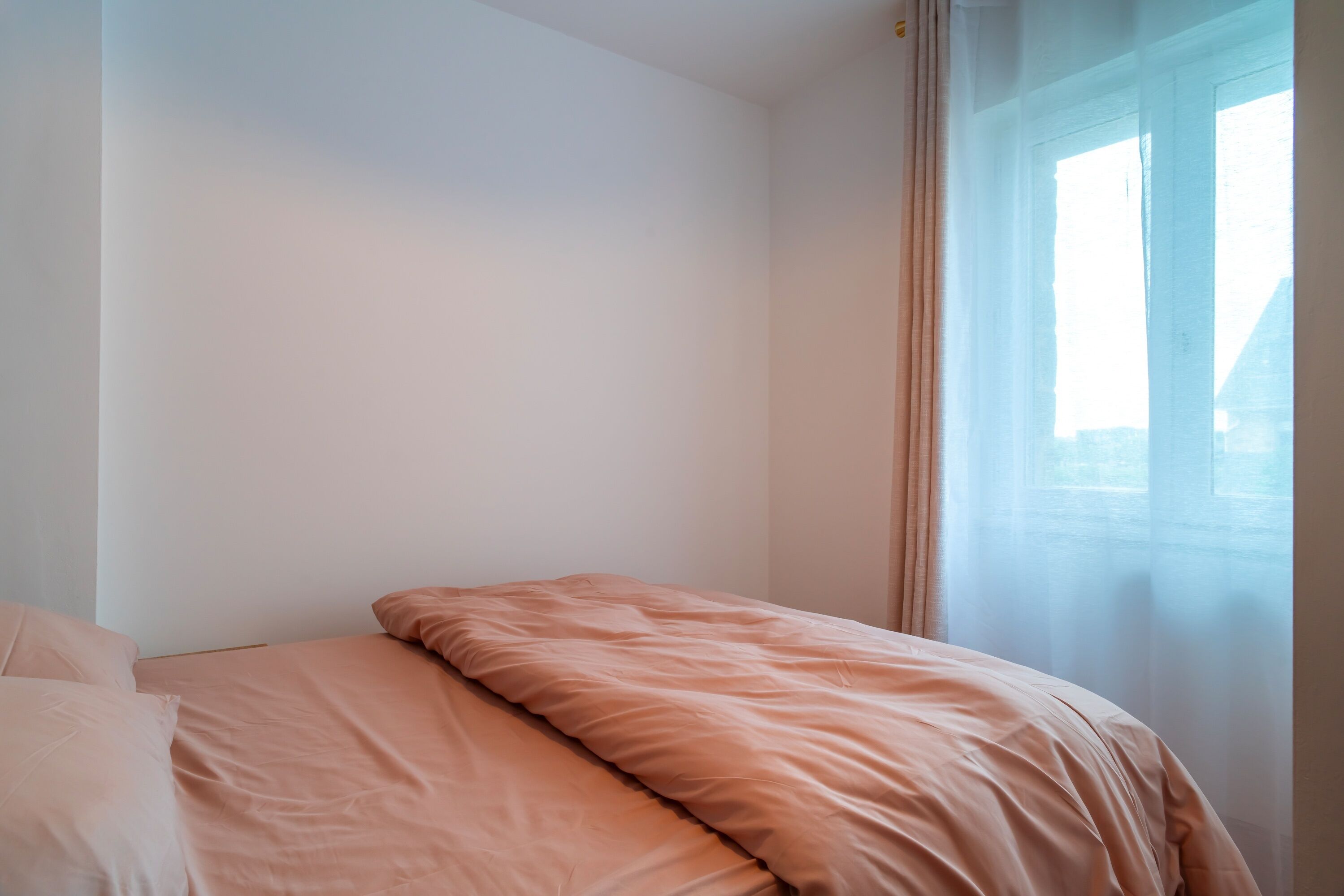 A bedroom with a bed, a window with curtains, and a view of the outside.