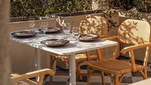 An outdoor dining area with a table set for four, surrounded by wicker chairs, under a stone archway. - Hotel Sevilla (Mérida)