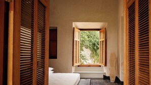 A bedroom with a bed, bench, and a window with wooden shutters. - Hotel Sevilla (Mérida)