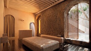 A modern spa room with a stone wall, a wooden ceiling, and a large window with bars. - Hotel Sevilla (Mérida)