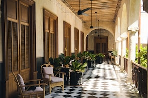 Um corredor com piso xadrez, persianas de madeira e plantas em vasos.