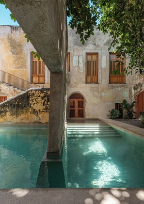A courtyard with a pool, stone walls, wooden shutters, and a staircase. - Hotel Sevilla (Mérida)