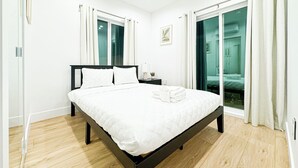 A modern bedroom with a large bed, a bedside table, a small plant, and a view through a glass door.