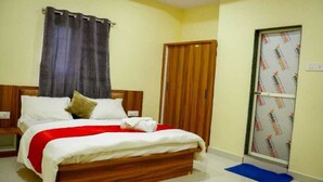 A bedroom with a wooden bed, white bedding, a red blanket, a wooden wardrobe, and a door with insulation. - Sai Residency  (Mahabaleshwar)