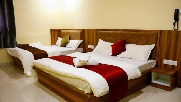 A double bed with a wooden headboard, two bedside tables, and a red accent pillow. - Sai Residency  (Mahabaleshwar)