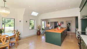 A spacious kitchen with a central island, large windows, and a dining area with wooden furniture. - Leafield Cottage (Gloucester)
