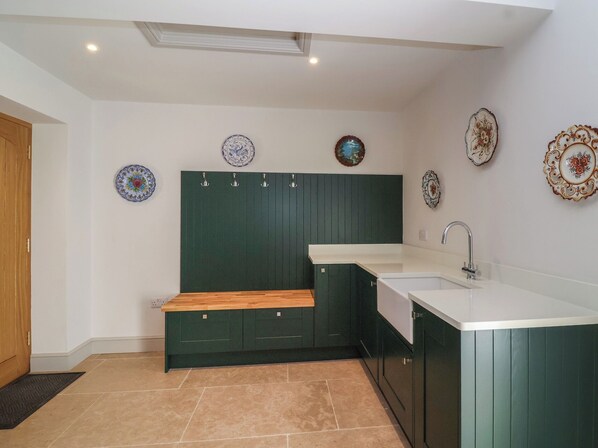 A compact kitchen with green cabinetry, a wooden bench, and decorative plates on the wall.