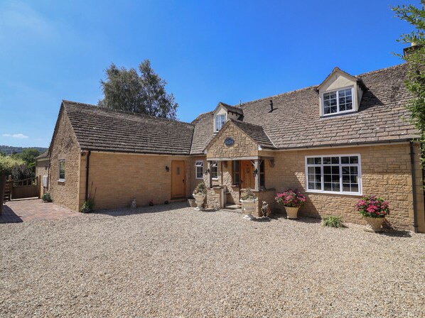 A stone house with a gravel driveway, a wooden gate, and a small garden with potted plants.
