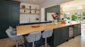 A modern kitchen with a wooden island, bar stools, and a view of the garden. - Leafield Cottage (Gloucester)