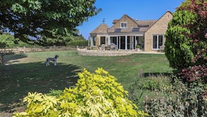 A stone house with a large lawn, a dog, and various plants. - Leafield Cottage (Gloucester)
